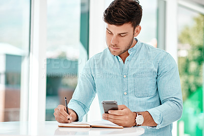 Buy stock photo Cropped shot of a handsome young businessman making notes while siting at a table in his office