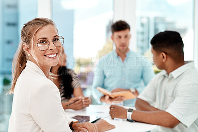Buy stock photo Cropped portrait of an attractive young woman sitting at a table with her colleagues in the office