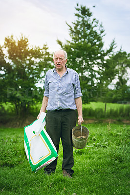 Buy stock photo Shot of a senior man holding a bag of animal feed on a farm