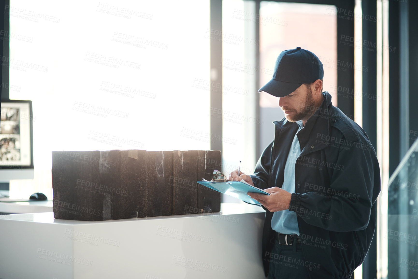 Buy stock photo Shot of a handsome delivery man writing on his clipboard while waiting in the lobby with a customer's order