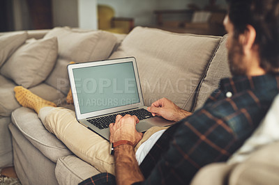Buy stock photo Shot of a handsome young man using his laptop while relaxing on a couch at home