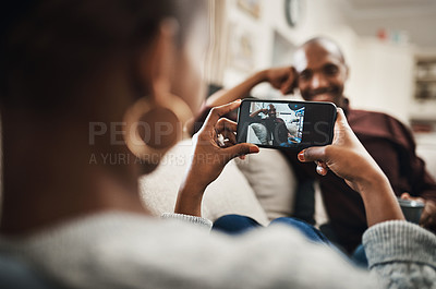 Buy stock photo Shot of a handsome young man posing for the camera while his girlfriends takes pictures of hime with her cellphone at home