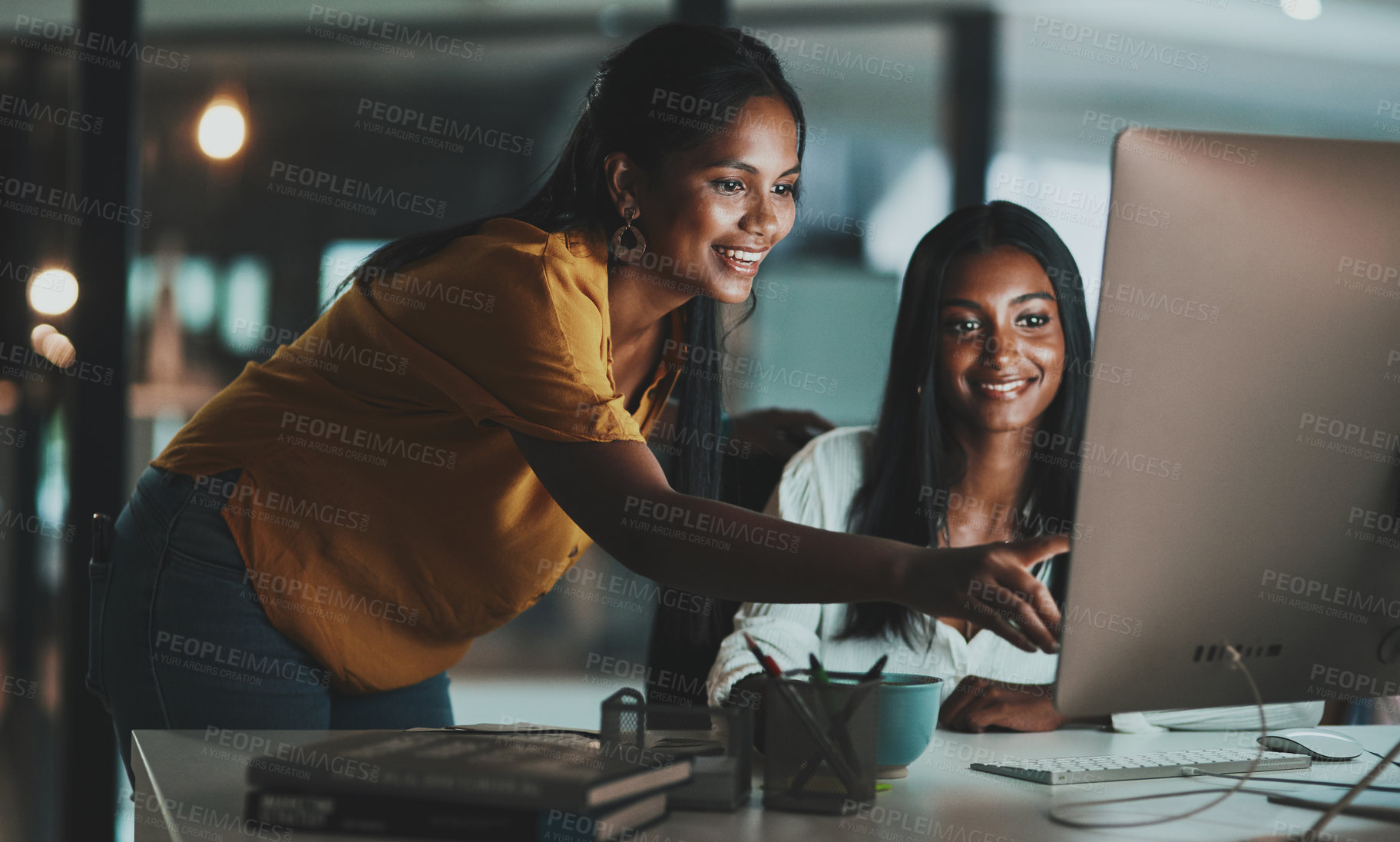 Buy stock photo Shot of two young businesswomen working together on a computer in an office at night