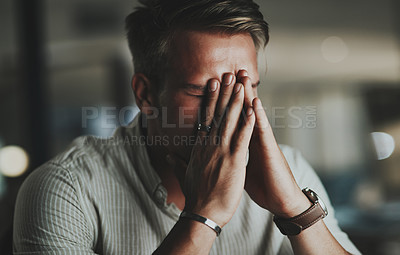 Buy stock photo Shot of a young businessman looking stressed out while working in an office at night