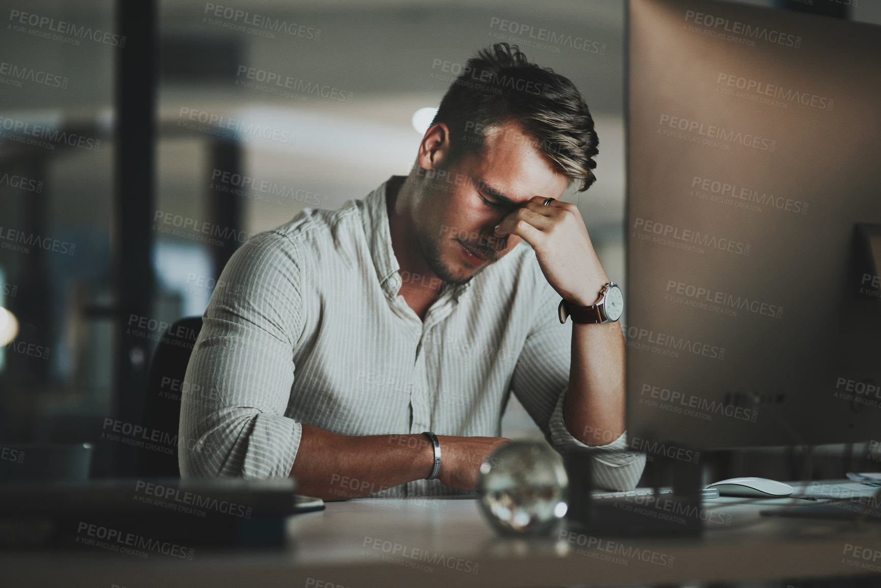 Buy stock photo Shot of a young businessman looking stressed out while working on a computer in an office at night