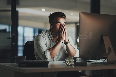 Buy stock photo Shot of a young businessman looking stressed out while working on a computer in an office at night