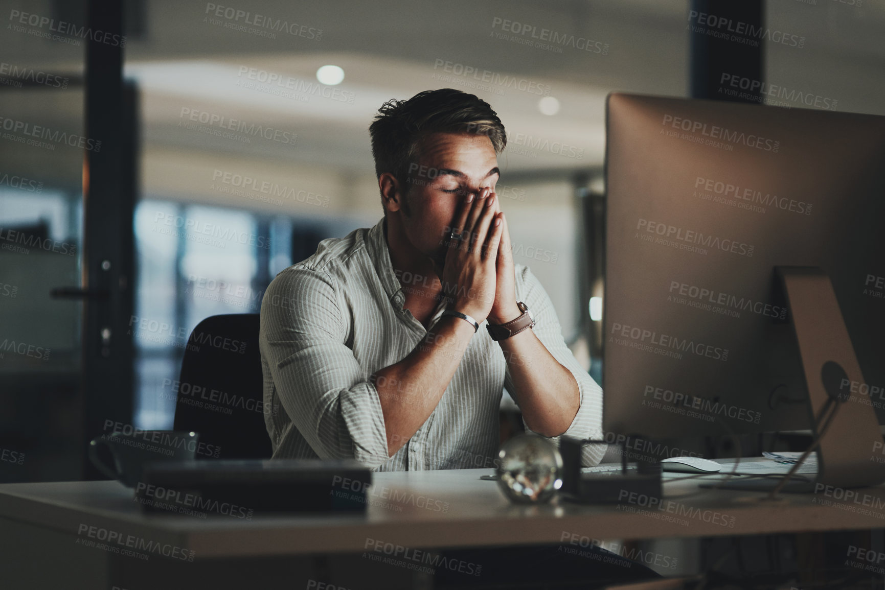 Buy stock photo Shot of a young businessman looking stressed out while working on a computer in an office at night