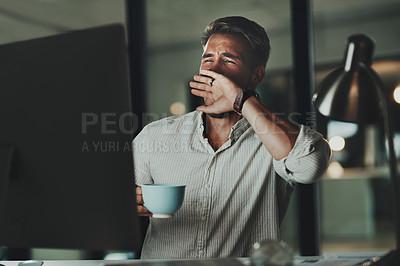 Buy stock photo Shot of a young businessman yawning while working on a computer in an office at night