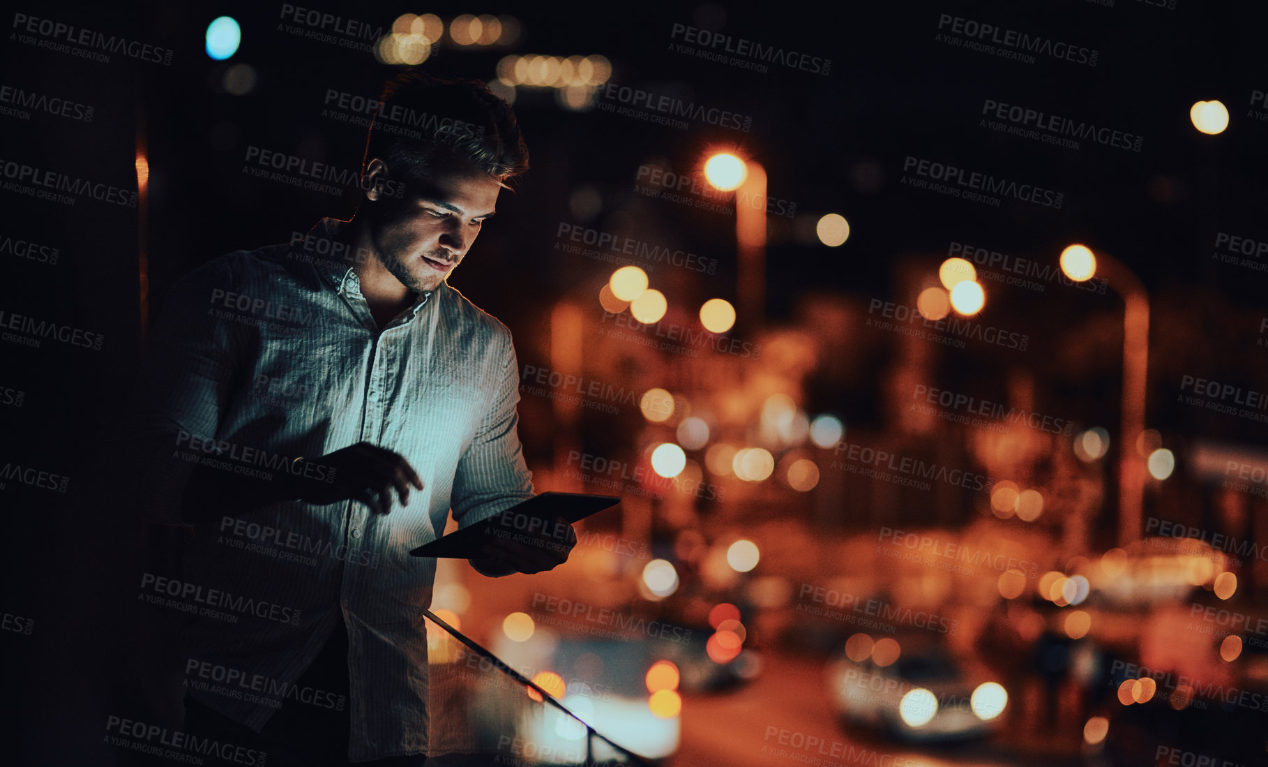 Buy stock photo Shot of a young businessman using a digital tablet outside an office at night