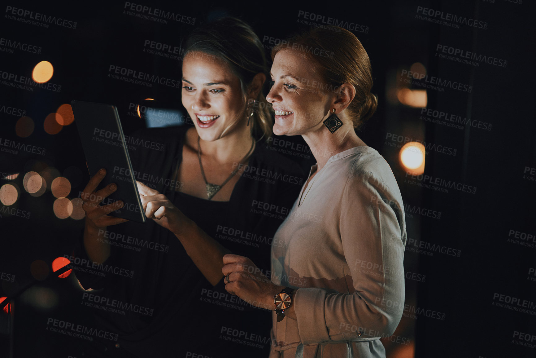 Buy stock photo Shot of two businesswomen using a digital tablet together outside an office at night