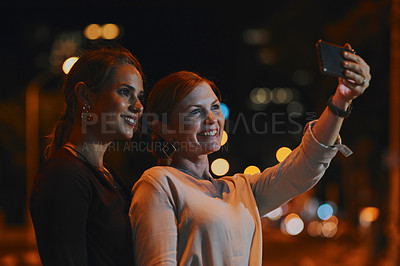 Buy stock photo Shot of two businesswomen taking selfies together outside an office at night