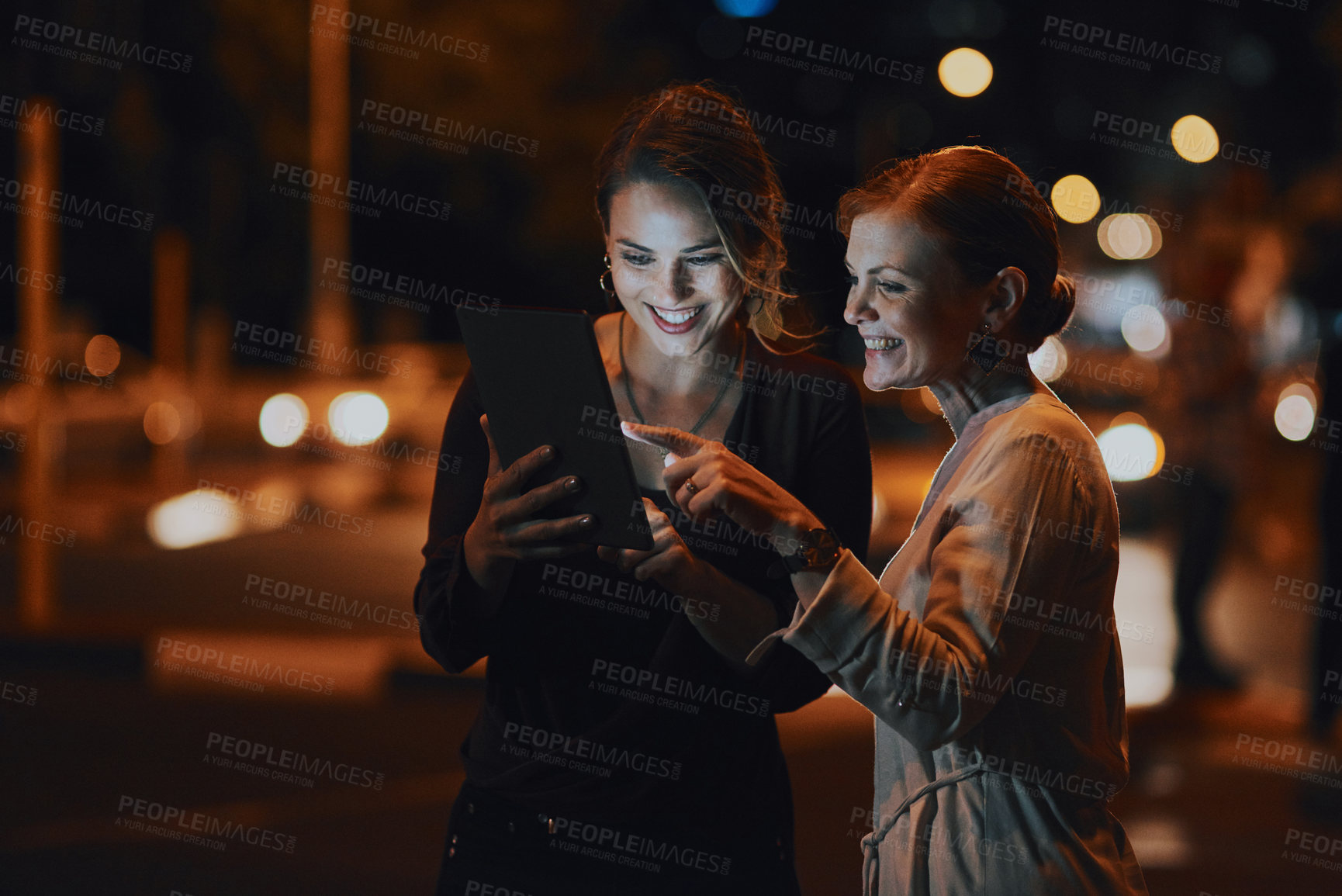 Buy stock photo Shot of two businesswomen using a digital tablet together outside an office at night