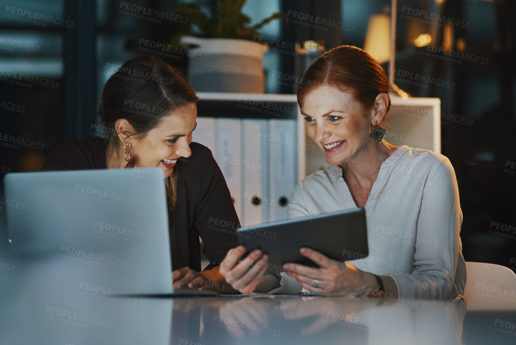 Buy stock photo Office, women and happy at night with technology for online research on deadline or overtime for project. People, employees and laptop or tablet for teamwork, collaboration and coworking for business