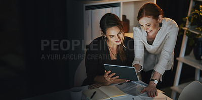 Buy stock photo Shot of two businesswomen using a digital tablet together in an office at night