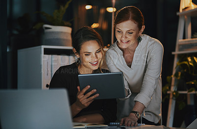 Buy stock photo Shot of two businesswomen using a digital tablet together in an office at night