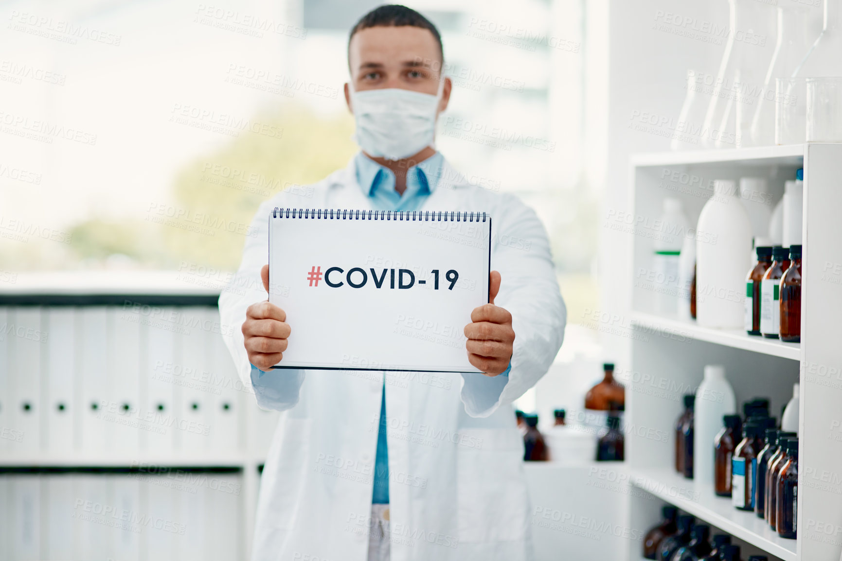 Buy stock photo Portrait of a young scientist holding a sign with “#COVID-19” on it in a modern laboratory
