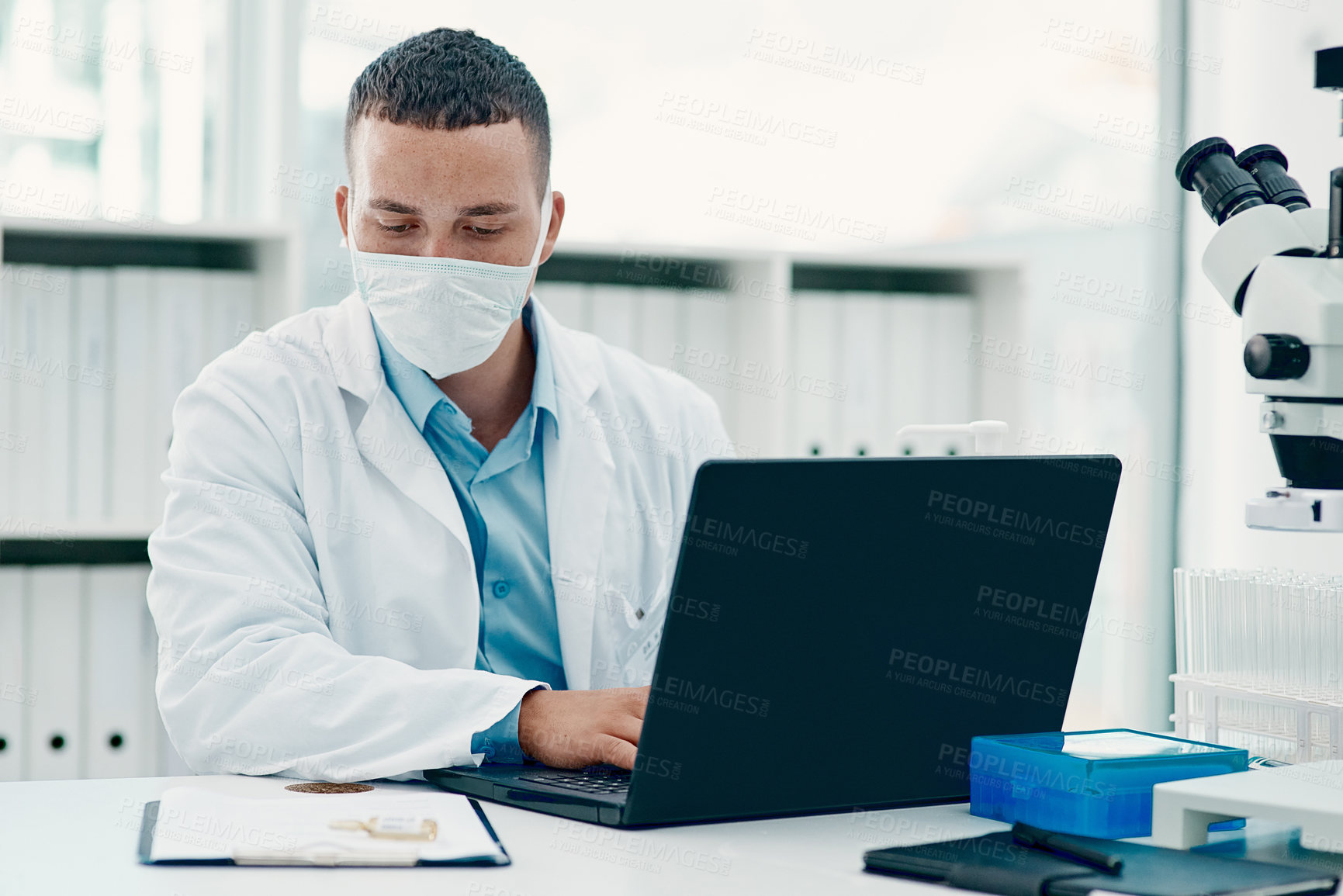 Buy stock photo Shot of a young scientist using a laptop while working on a coronavirus cure in a laboratory