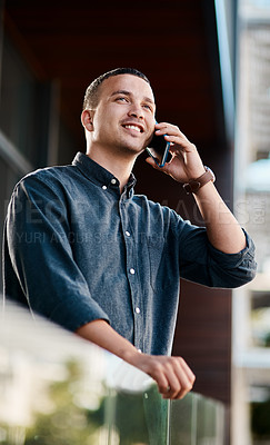 Buy stock photo Shot of a young businessman standing on an office balcony and using a smartphone