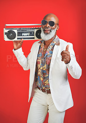 Buy stock photo Studio shot of a senior man wearing vintage clothing while posing with a boombox against a red background
