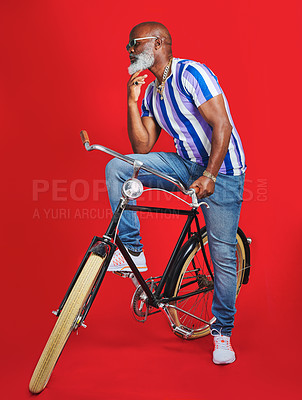 Buy stock photo Shot of a senior man sitting on a vintage bicycle against a red background