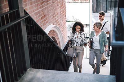 Buy stock photo Shot of two businesswomen having a discussion while walking up the stairs in a modern workplace