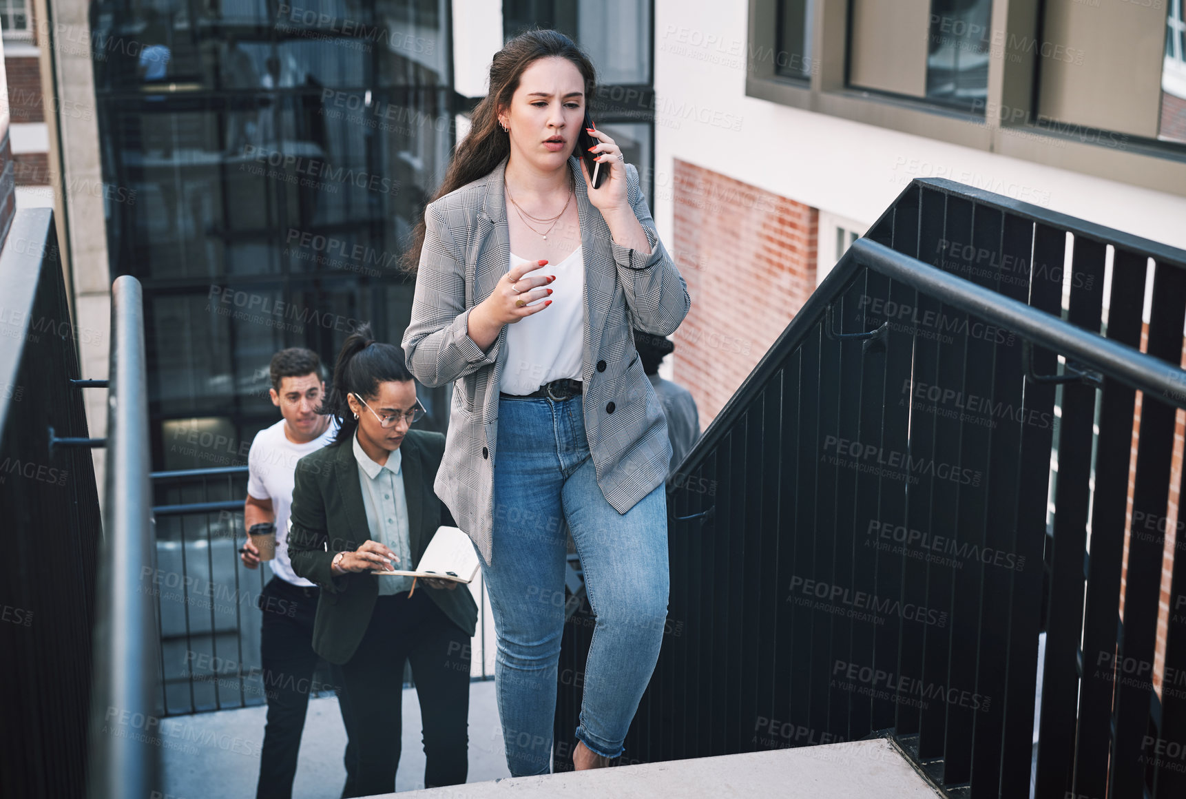 Buy stock photo Shot of a young businesswoman looking using a smartphone while walking up the stairs in a modern workplace