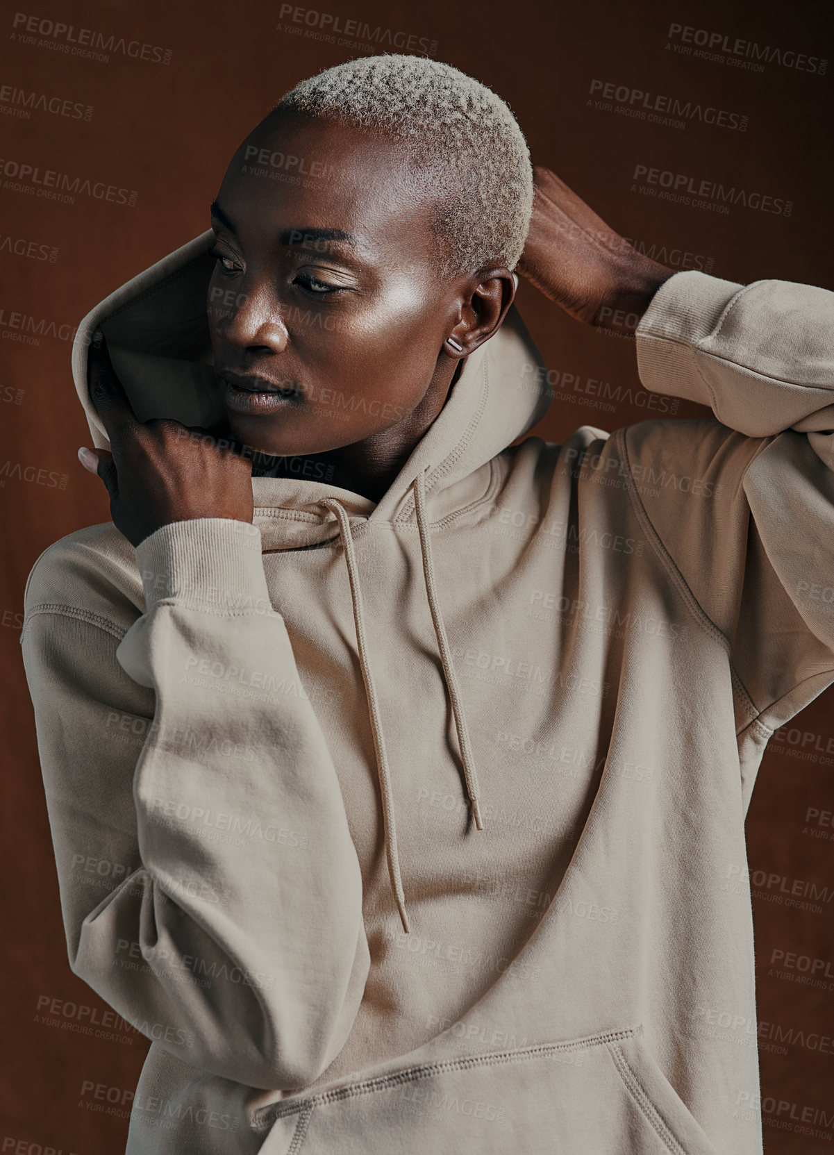 Buy stock photo Studio shot of an attractive young woman wearing a hoodie and posing against a brown background