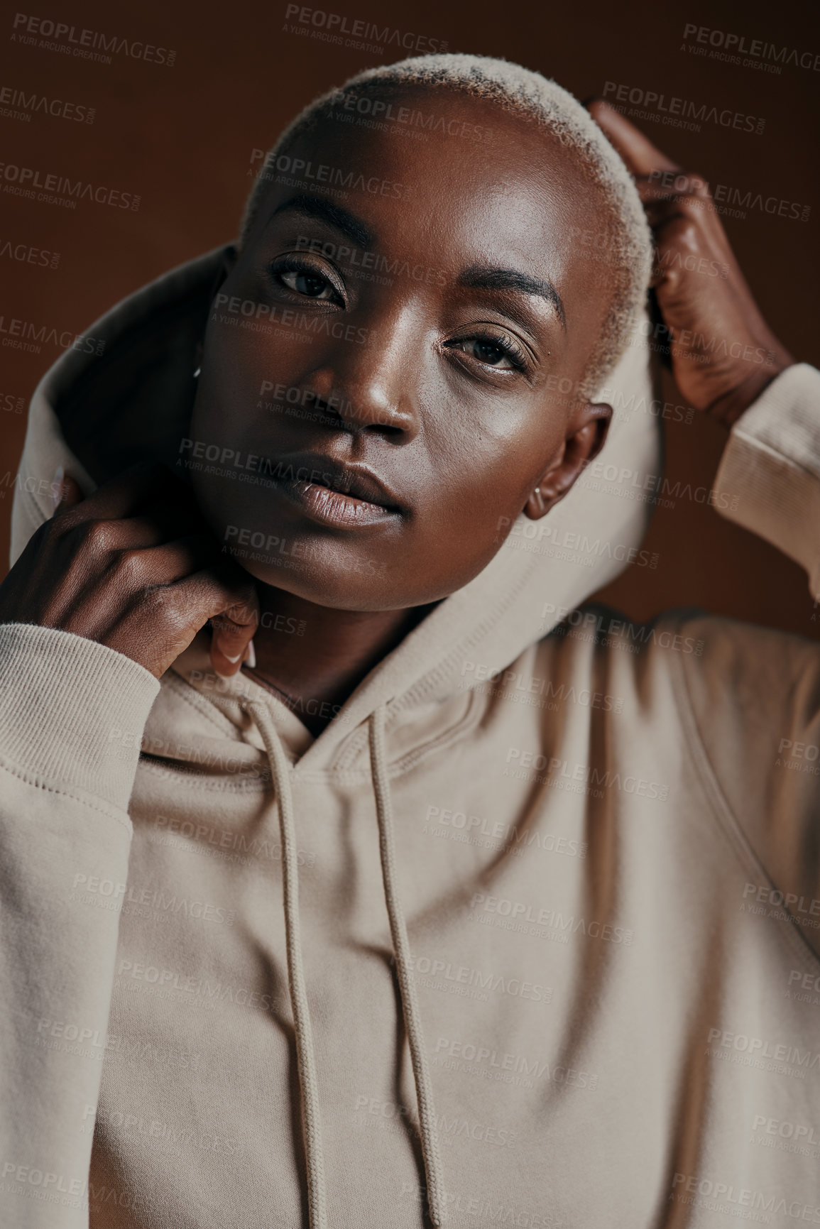 Buy stock photo Studio portrait of an attractive young woman wearing a hoodie and posing against a brown background