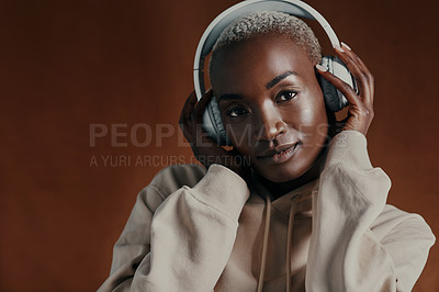 Buy stock photo Studio portrait of an attractive young woman wearing headphones and posing against a brown background