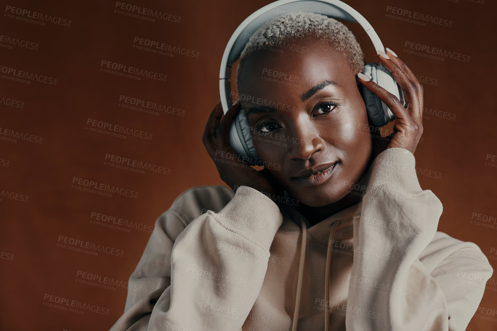 Buy stock photo Studio portrait of an attractive young woman wearing headphones and posing against a brown background