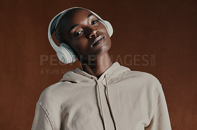 Buy stock photo Studio portrait of an attractive young woman wearing headphones and posing against a brown background