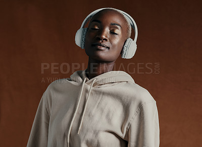 Buy stock photo Studio shot of an attractive young woman wearing headphones and posing against a brown background