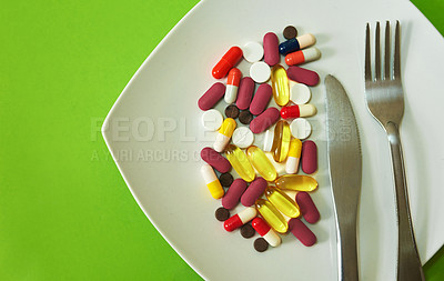 Buy stock photo Studio shot of medication served on a plate with a fork and knife against a green background