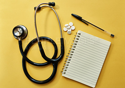 Buy stock photo Studio shot of a stethoscope, notepad, pen and pills against a yellow background