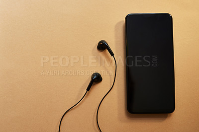 Buy stock photo Studio shot of a smartphone and earphones against a brown background
