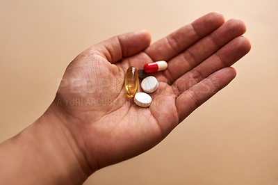 Buy stock photo Studio shot of an unrecognisable woman holding a handful of pills against a brown background