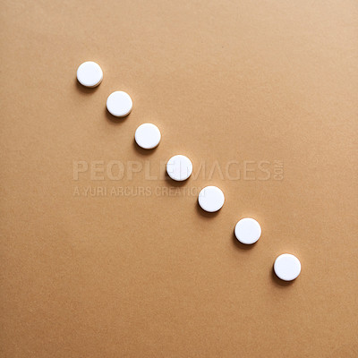Buy stock photo Studio shot of a row of white tablets against a brown background