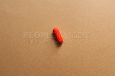 Buy stock photo Studio shot of a single red capsule against a brown background