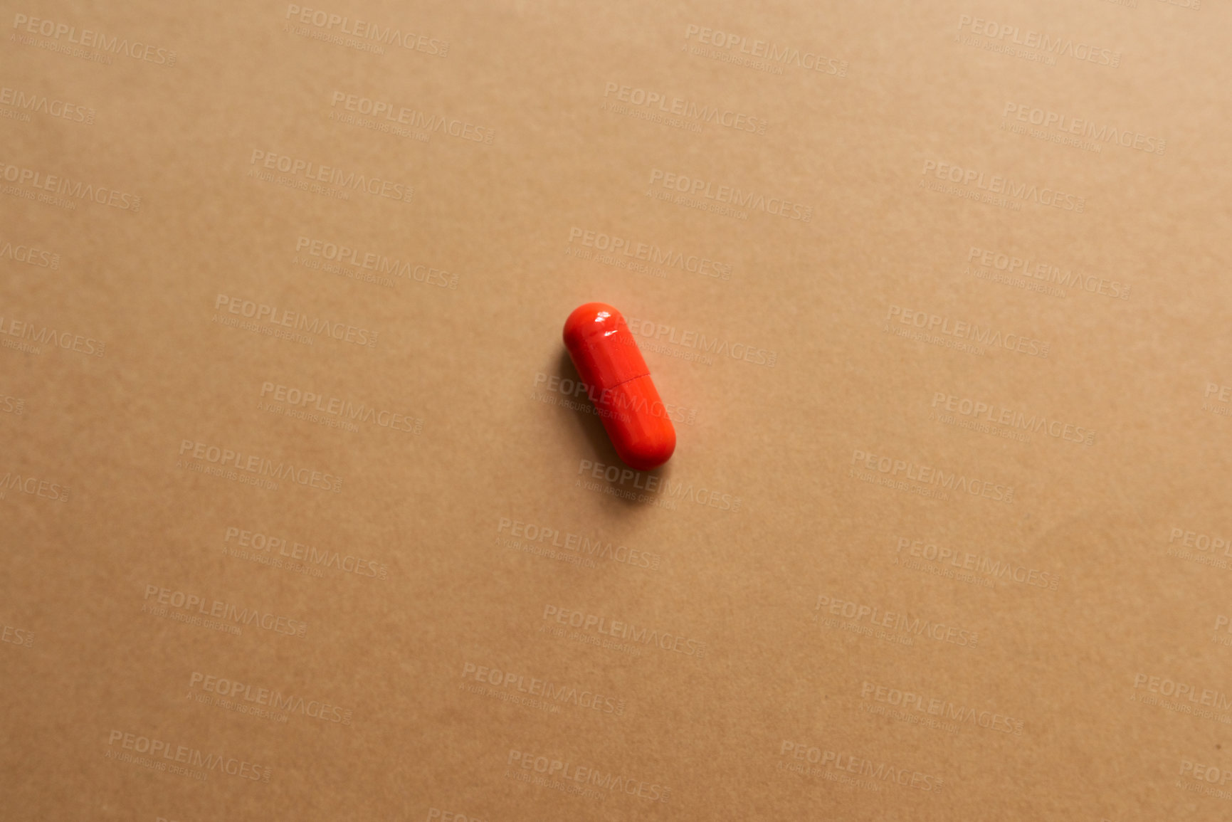 Buy stock photo Studio shot of a single red capsule against a brown background