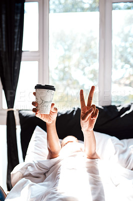 Buy stock photo Cropped shot of a woman lying in the covers whole holding up a coffee and showing the peace sign