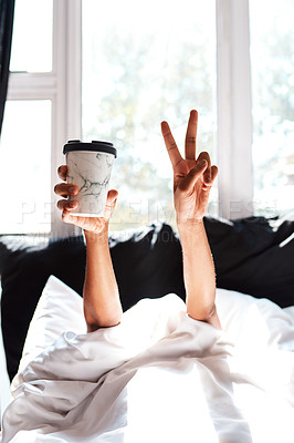 Buy stock photo Cropped shot of a woman lying in the covers whole holding up a coffee and showing the peace sign