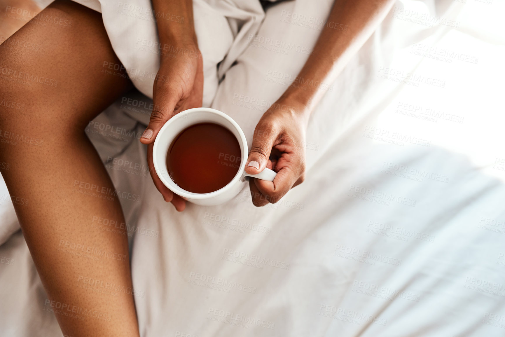 Buy stock photo Cropped shot of an unrecognizable woman holding a cup of team while sitting on her bed