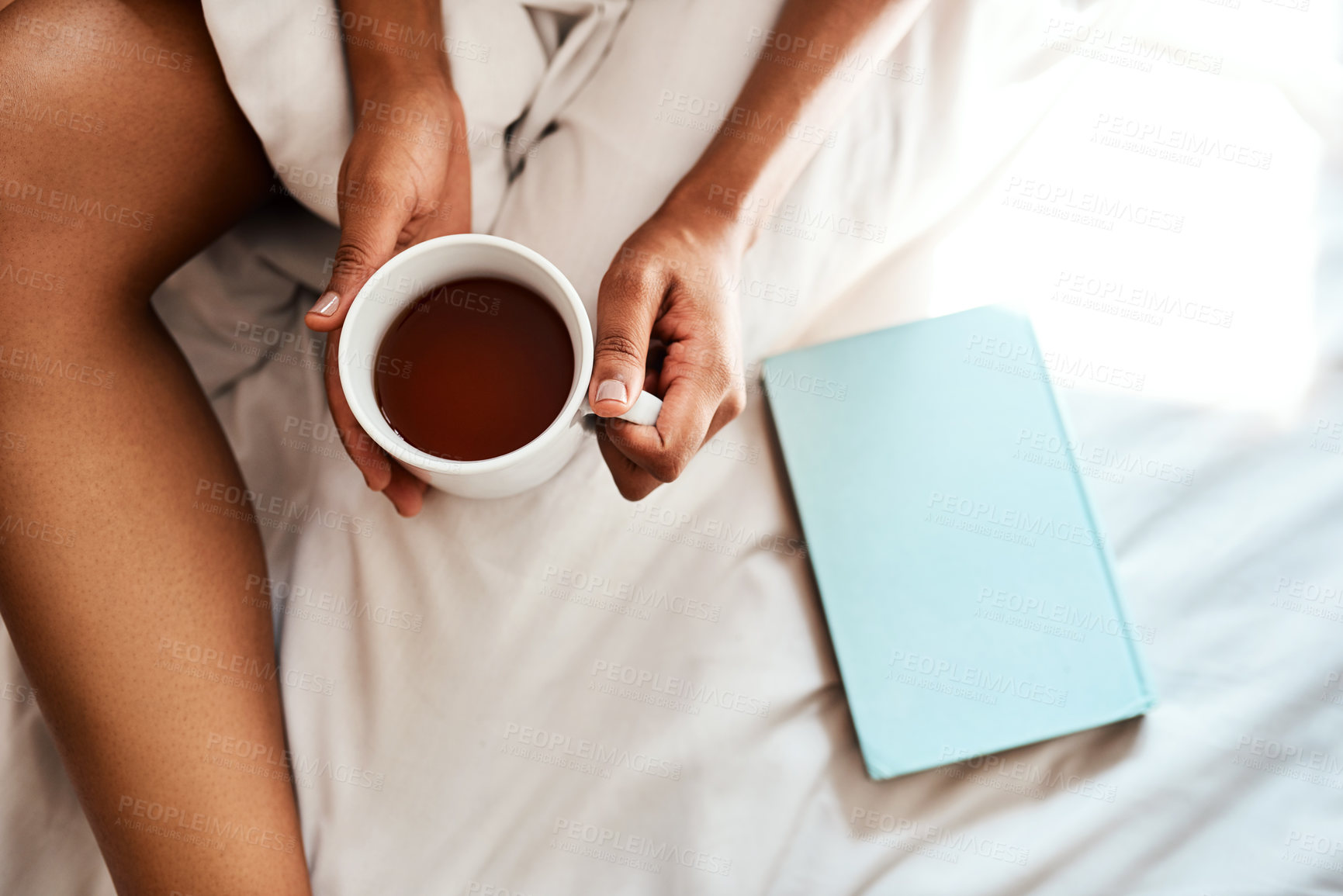 Buy stock photo Cropped shot of an unrecognizable woman sitting on her bed with tea and a book