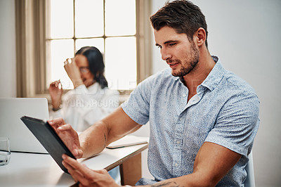 Buy stock photo Shot of a young businessman using a digital tablet during a meeting in a modern office