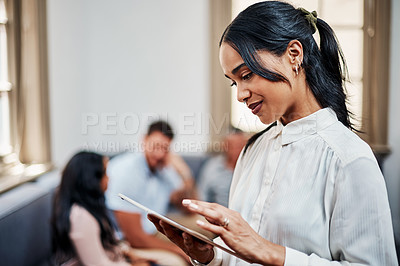 Buy stock photo Shot of a young businesswoman using a digital tablet with her colleagues in the background