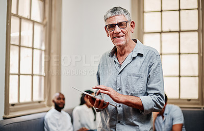 Buy stock photo Shot of a mature businessman using a digital tablet with his colleagues in the background