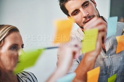 Buy stock photo Cropped shot of two business colleagues brainstorming on a glass wipe board in their office