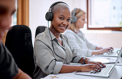 Buy stock photo Portrait of a young businesswoman wearing headphones while working on a laptop alongside her colleagues in an office