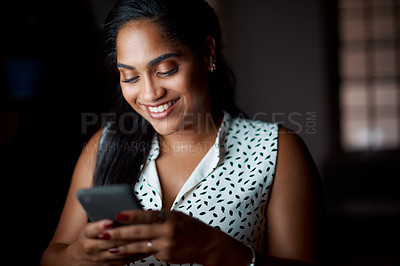 Buy stock photo Shot of a young businesswoman using a cellphone in an office at night