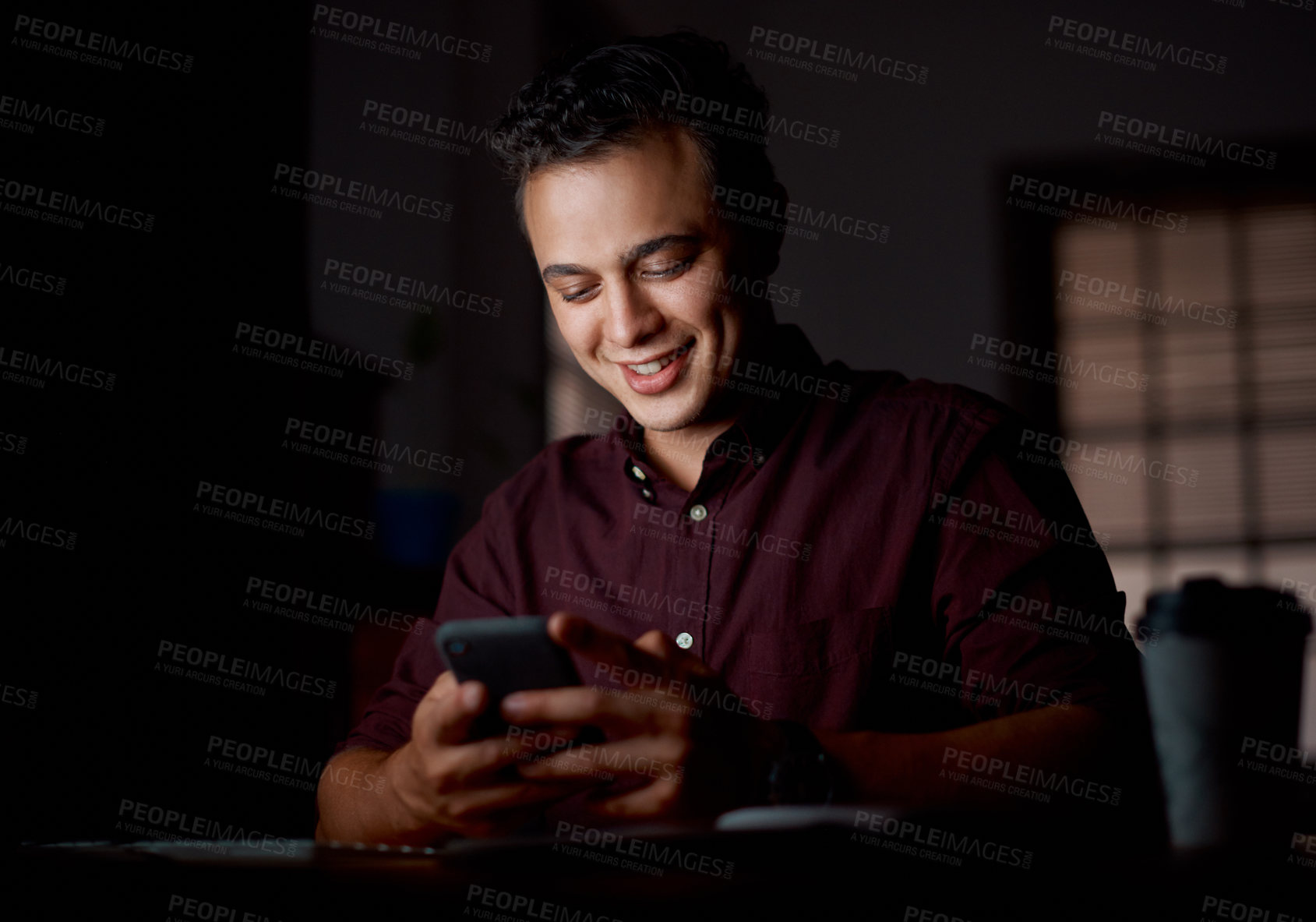 Buy stock photo Shot of a young businessman using a cellphone in an office at night